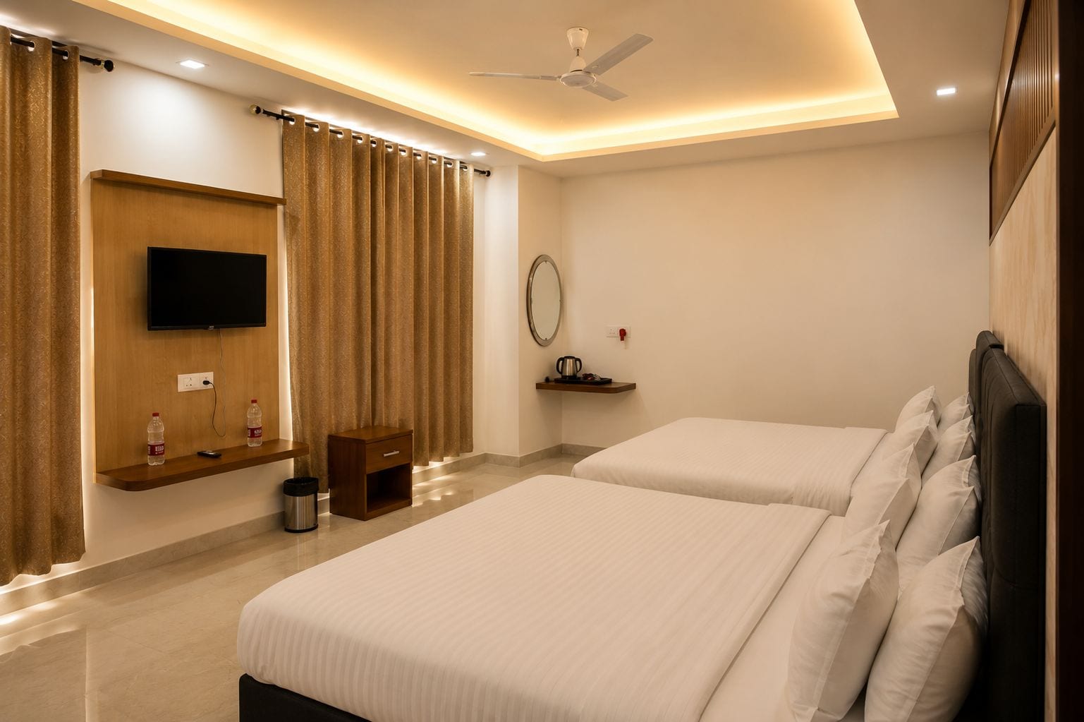 A hotel room with two beds, a TV, a ceiling fan, a small table, and a shelf with a kettle.