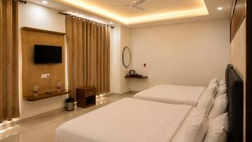 A hotel room with two beds, a TV, a ceiling fan, a small table, and a shelf with a kettle.