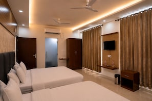 A hotel room with two beds, a TV, a ceiling fan, and a window with curtains. - Hotel Maurya Greens (Purnagiri)