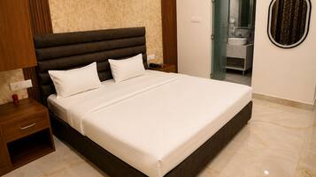 Una habitación de hotel moderna con una cama grande, una mesita de noche y un baño visible a través de una puerta abierta.