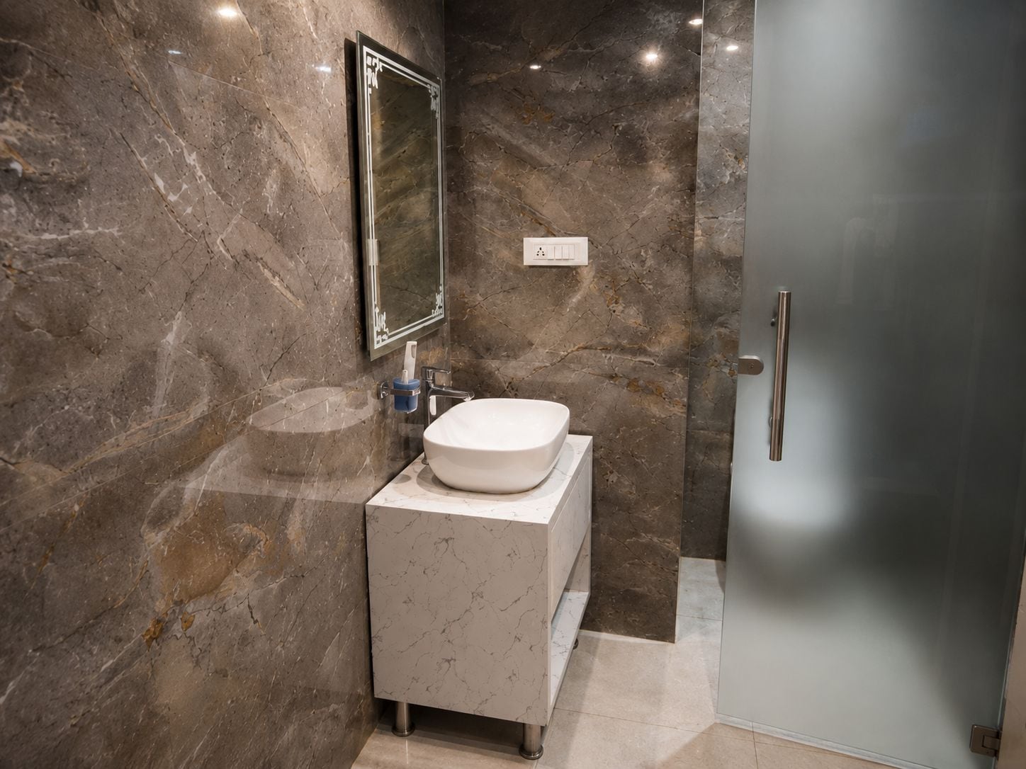A bathroom with a marble wall, a white sink, and a glass shower door.