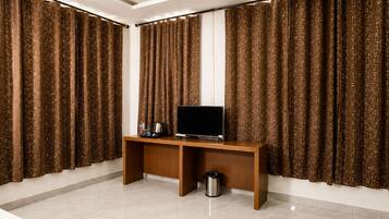 Una habitación con un escritorio de madera, un televisor y cortinas.