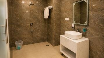 Un baño con pared de mármol, un lavamanos, un espejo y una ducha.