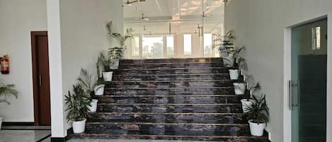 A marble-floored staircase with potted plants on either side, leading to a glass door entrance.