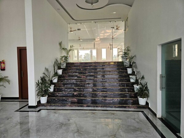 A marble-floored staircase with potted plants on either side, leading to a glass door entrance. - Hotel Maurya Greens (Purnagiri)