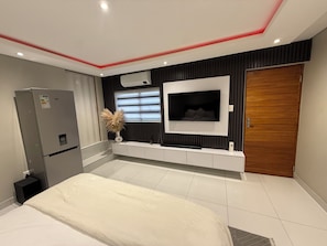 A modern bedroom with a bed, a television mounted on the wall, a built-in wardrobe, and a refrigerator. - Private & Modern Studio Apartment in Sandton (Johannesburg)