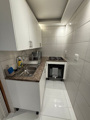 A modern kitchen with white cabinets, a granite countertop, stainless steel sink, and a built-in oven. - Private & Modern Studio Apartment in Sandton (Johannesburg)