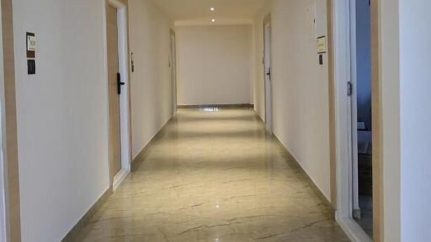 Un pasillo largo y estrecho con suelo de mármol y paredes blancas, que conduce a una puerta al final.