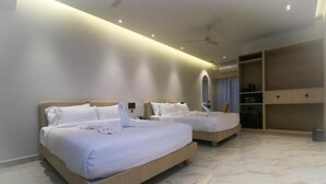 Une chambre d’hôtel avec deux lits, un ventilateur de plafond, un minibar et un grand miroir.