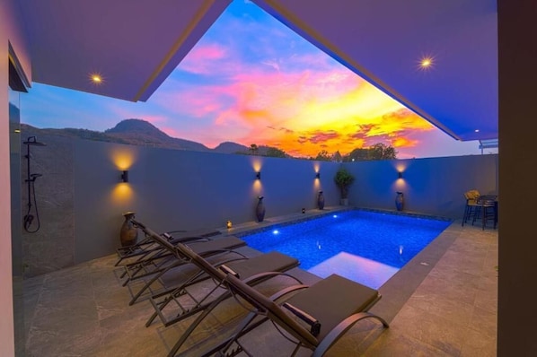 Ein Pool mit Liegestühlen, Blick auf den Sonnenuntergang und Wandleuchten.