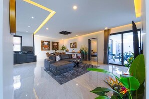 A modern living room with a sofa, a coffee table, and a dining area with chairs. - Luxury Modern Pool Villa 2BR - KL2 (Hua Hin)