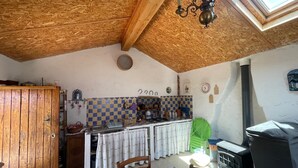 Une cuisine rustique avec un plafond en bois, une table à manger recouverte d’une nappe à motifs floraux et une chaise verte.