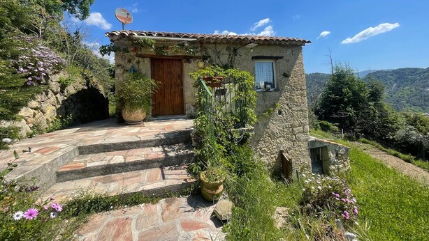 Une maison en pierre avec une porte en bois, une petite fenêtre et une antenne parabolique.