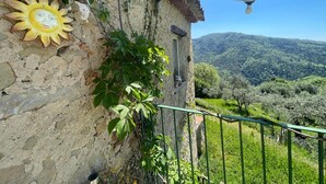 Un bâtiment rustique en pierre, orné d’un motif solaire, avec une lampe en métal et une vue sur une vallée verdoyante.