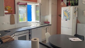 Keittiössä on ikkuna, jääkaappi, pesuallas sekä ruokailutila, jossa on pöytä ja tuolit.