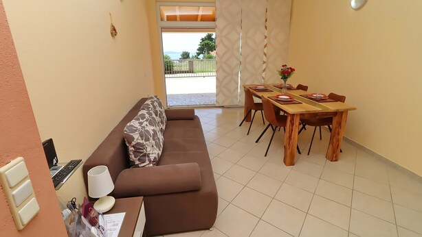 A living area with a sofa, a dining table set with chairs, a laptop on a side table, and a view through a sliding door. - Apartments Villa Michele-one Bedroom Apartment With Terrace (Orebic)