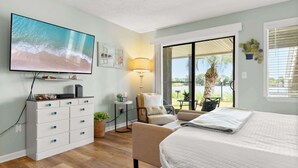 A bedroom with a TV, a desk, a chair, a bed, and a view of the outdoors. - Shore Thing - Studio Stay (Panama City Beach)