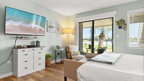 A bedroom with a TV, a desk, a chair, a bed, and a view of the outdoors. - Shore Thing - Studio Stay (Panama City Beach)