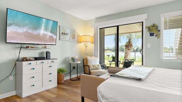 A bedroom with a TV, a desk, a chair, a bed, and a view of the outdoors. - Shore Thing - Studio Stay (Panama City Beach)