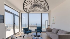 Ein modernes Wohnzimmer mit großen Fenstern, einer Deckenleuchte und Meerblick.
