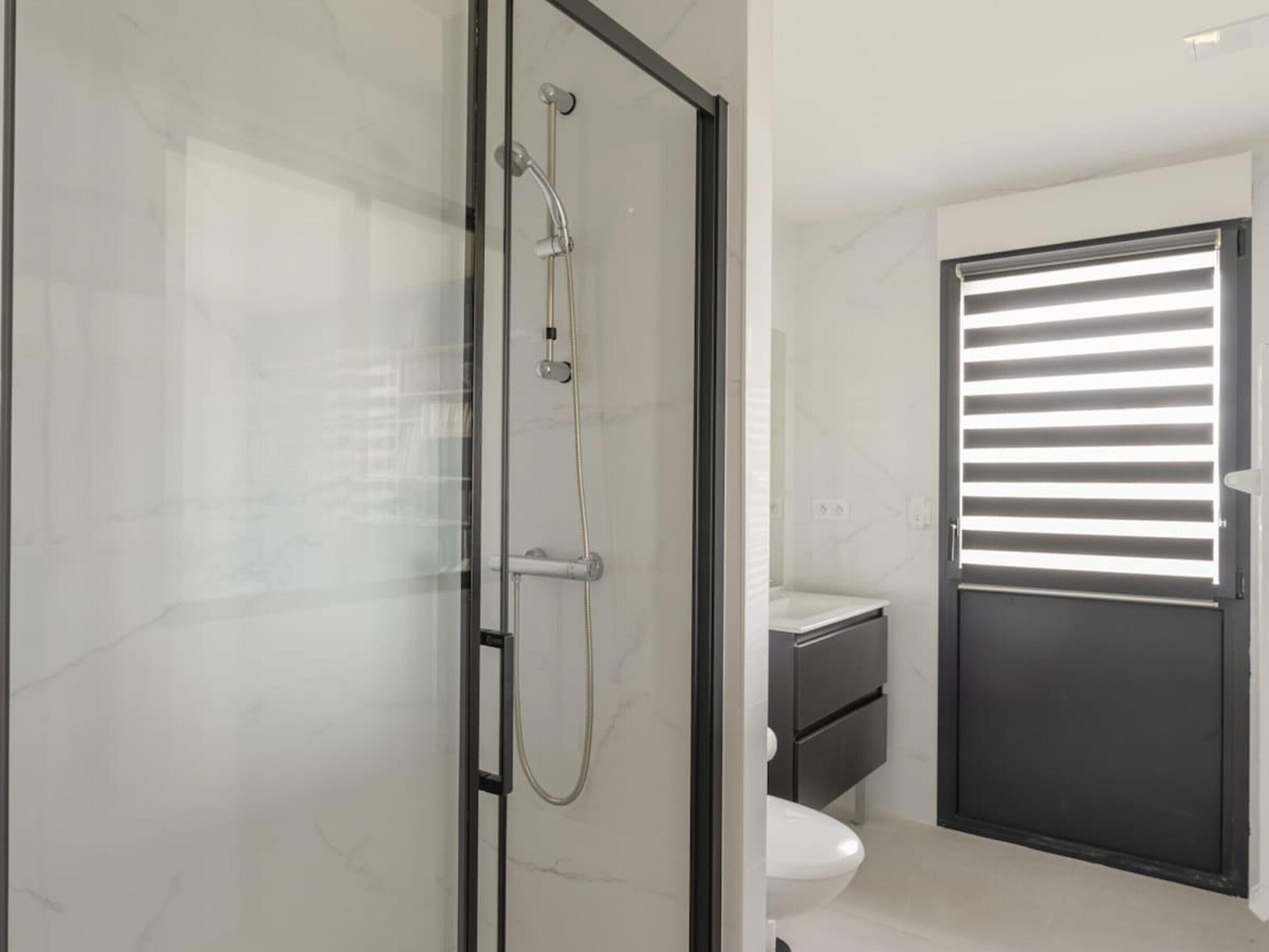 A modern bathroom with a glass shower enclosure, a toilet, and a sink.