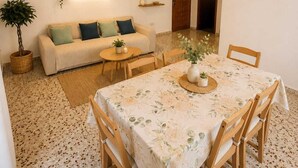 Una sala de estar acogedora con un sofá, una mesa redonda con sillas, una lámpara colgante y una puerta al fondo.