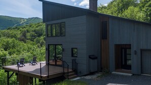 A modern two-story building with a deck, large windows, and a chimney.