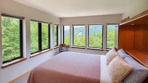 A bedroom with a large bed, multiple windows, a chair, and a wooden bench.