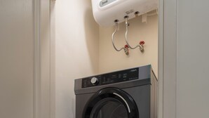 A stacked washer and dryer unit with control panels, a water heater above, and a white door. - Madison Grand Studio - King Bed - Pool & Gym access (Thành phố Hồ Chí Minh)