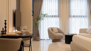 A modern living room with a sofa, armchair, dining table, and a TV. - Madison Grand Studio - King Bed - Pool & Gym access (Thành phố Hồ Chí Minh)