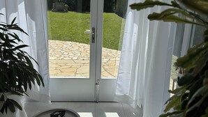 A room with a sliding glass door leading to a patio with a stone floor, a small table with a book and sunglasses, and a potted plant. - La Torre, Villa in Sant Martí d'Empúries (L'Escala)