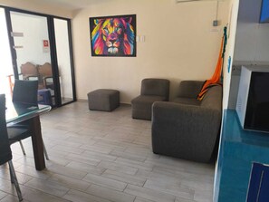 Ein Zimmer mit einem Glastisch, zwei grauen Sofas, einem kleinen Hocker und einem farbenfrohen Löwenbild an der Wand.
