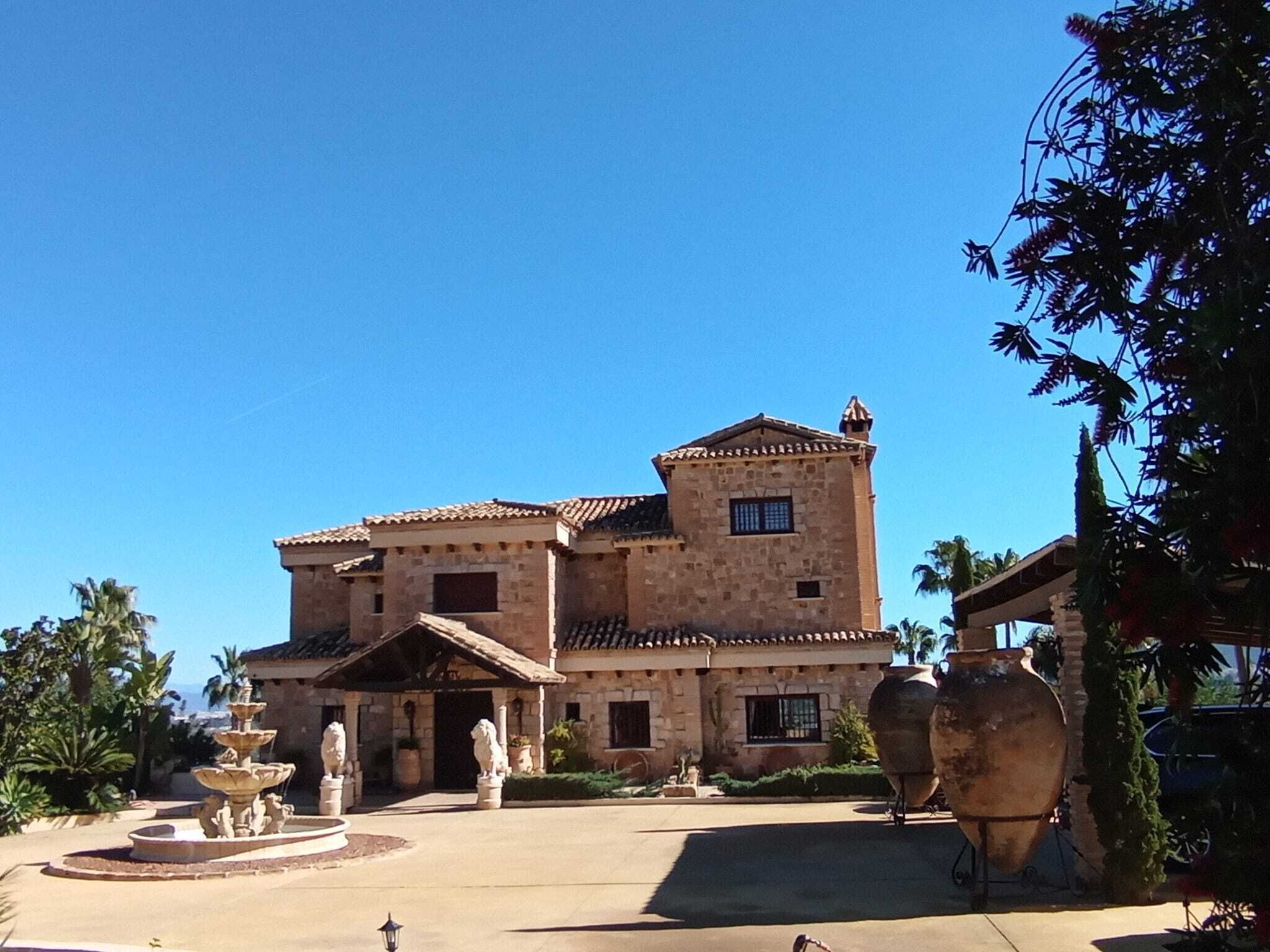 Um edifício grande de pedra com telhado ladrilhado, uma fonte e estátuas no pátio.