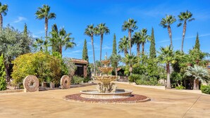 Un jardín con una fuente, palmeras y un edificio con techo de tejas.