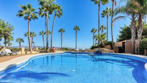 Una piscina con agua cristalina azul, rodeada de altas palmeras y sillas de descanso.