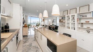 A modern kitchen with a central island, white cabinetry, and pendant lighting. - Absolute Waterfront Luxe Sub-Penthouse | 3BR | Panoramic Views (South Townsville)