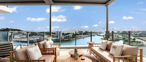 A balcony with a view of a marina, a round wooden table, and two sofas with cushions.