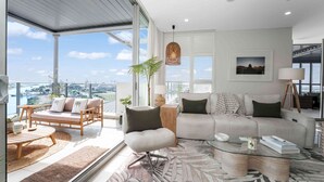 A spacious living room with a large window, a sofa, a coffee table, and a dining area. - Absolute Waterfront Luxe Sub-Penthouse | 3BR | Panoramic Views (South Townsville)