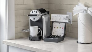 Eine Nespresso-Kaffeemaschine, eine Kaffeetasse, eine Taschentuchbox und ein Willkommensschild auf einer Küchenarbeitsplatte.