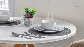 Ein runder Esstisch mit weißer Tischdecke, einer kleinen Topfpflanze, einem Glas und Besteck.