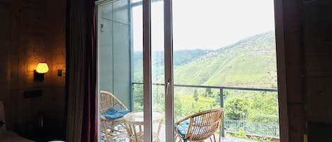 Un dormitorio con cama, mesita de noche, lámpara y vistas a un balcón con sillas y un paisaje pintoresco.