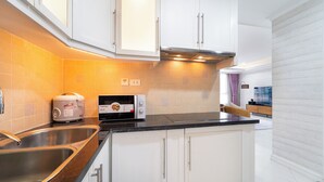 Uma cozinha moderna com armários brancos, bancada preta, pia de aço inoxidável e micro-ondas.