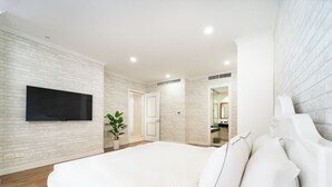 Quarto moderno com cama grande, paredes de tijolo branco, televisão de tela plana e banheiro visível por uma porta aberta.