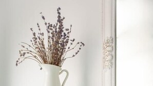 Pared blanca con azulejos, una estantería color turquesa con un florero de flores secas, un picaporte y un espejo decorativo.