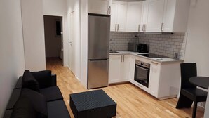 Een moderne keuken met witte kasten, een roestvrijstalen koelkast, een inbouwoven en een klein eethoekje met een zwarte stoel.