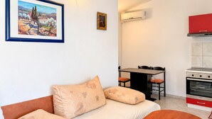 A living room with a sofa, a painting, a clock, a dining table with chairs, and a kitchen area with a stove and oven. - 1 bedroom beautiful apartment in Sabunike (Sabunike)