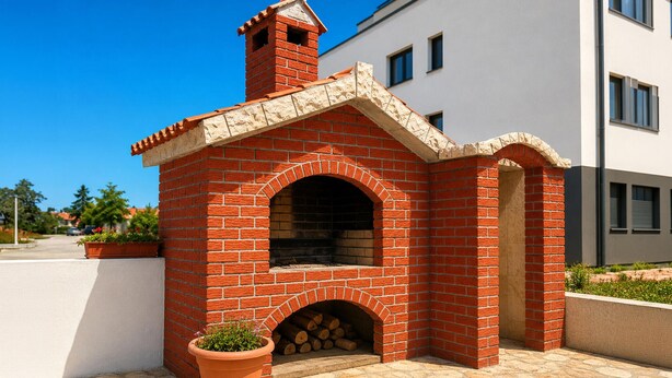 Una pequeña construcción de ladrillo al aire libre con una chimenea, una ventana y una puerta, junto a un edificio moderno.