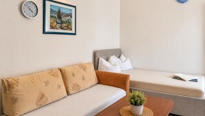 Una sala moderna con un sofá, un sillón adicional, una mesa de centro con una planta, un reloj y un cuadro en la pared.