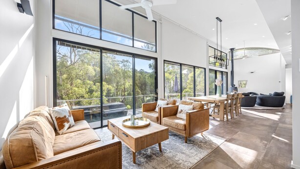 A spacious living area with large windows, a wooden coffee table, leather sofas, and a dining area with chairs.