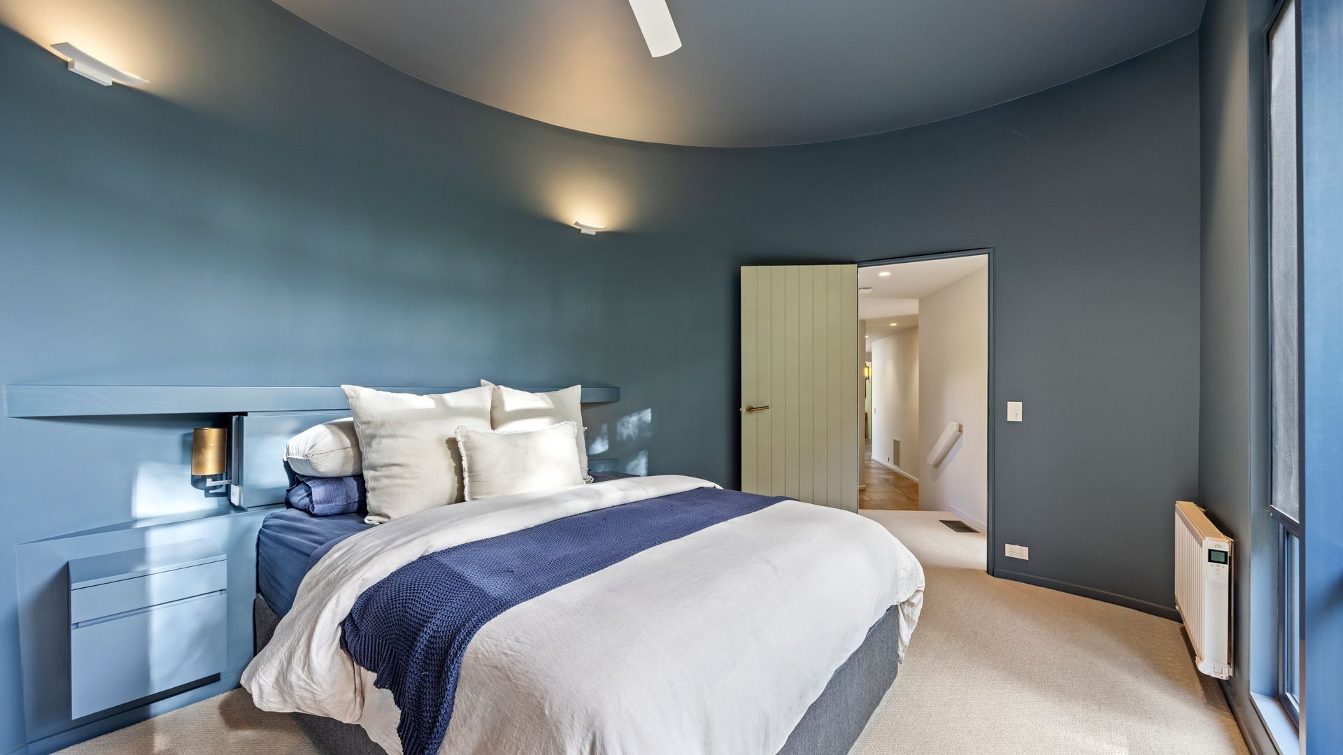 A bedroom with a curved ceiling, a bed with a blue and white bedspread, bedside tables, and a nightstand.